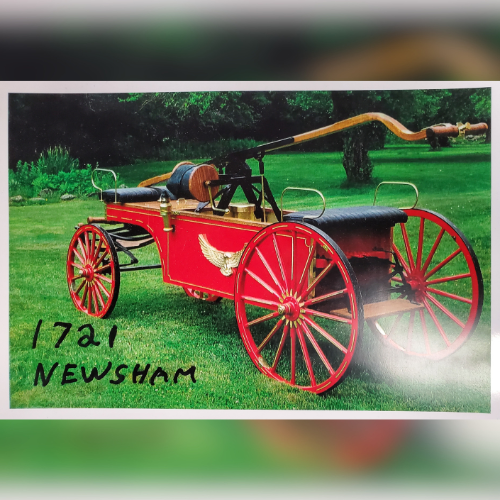 A historic red Newsham fire engine from 1721 with large wooden wheels and a handle, displayed on a grassy lawn, evoking a sense of vintage charm.